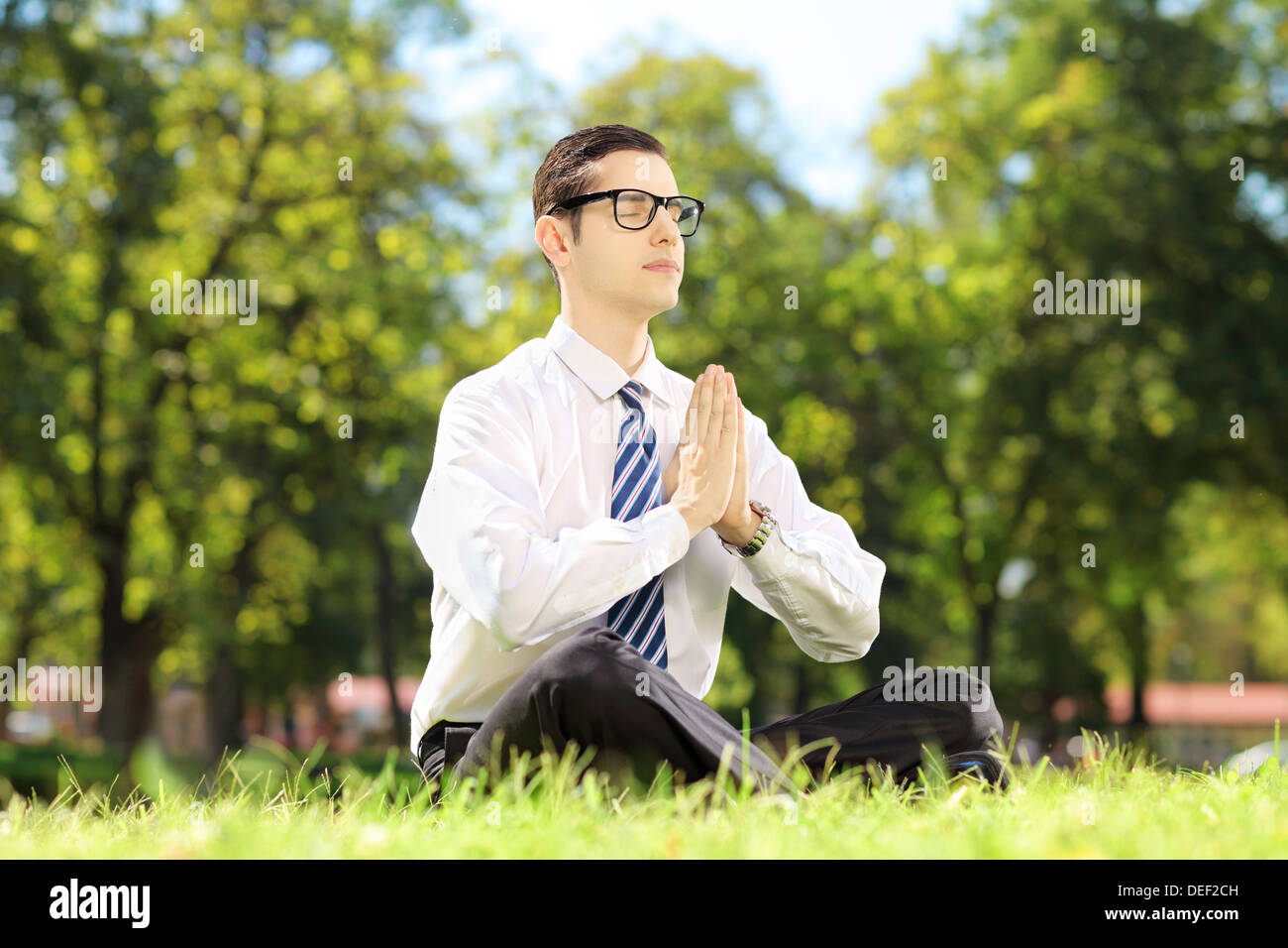 Junge Unternehmer mit Brille Yoga Übung sitzen auf einer Wiese in einem park Stockfoto