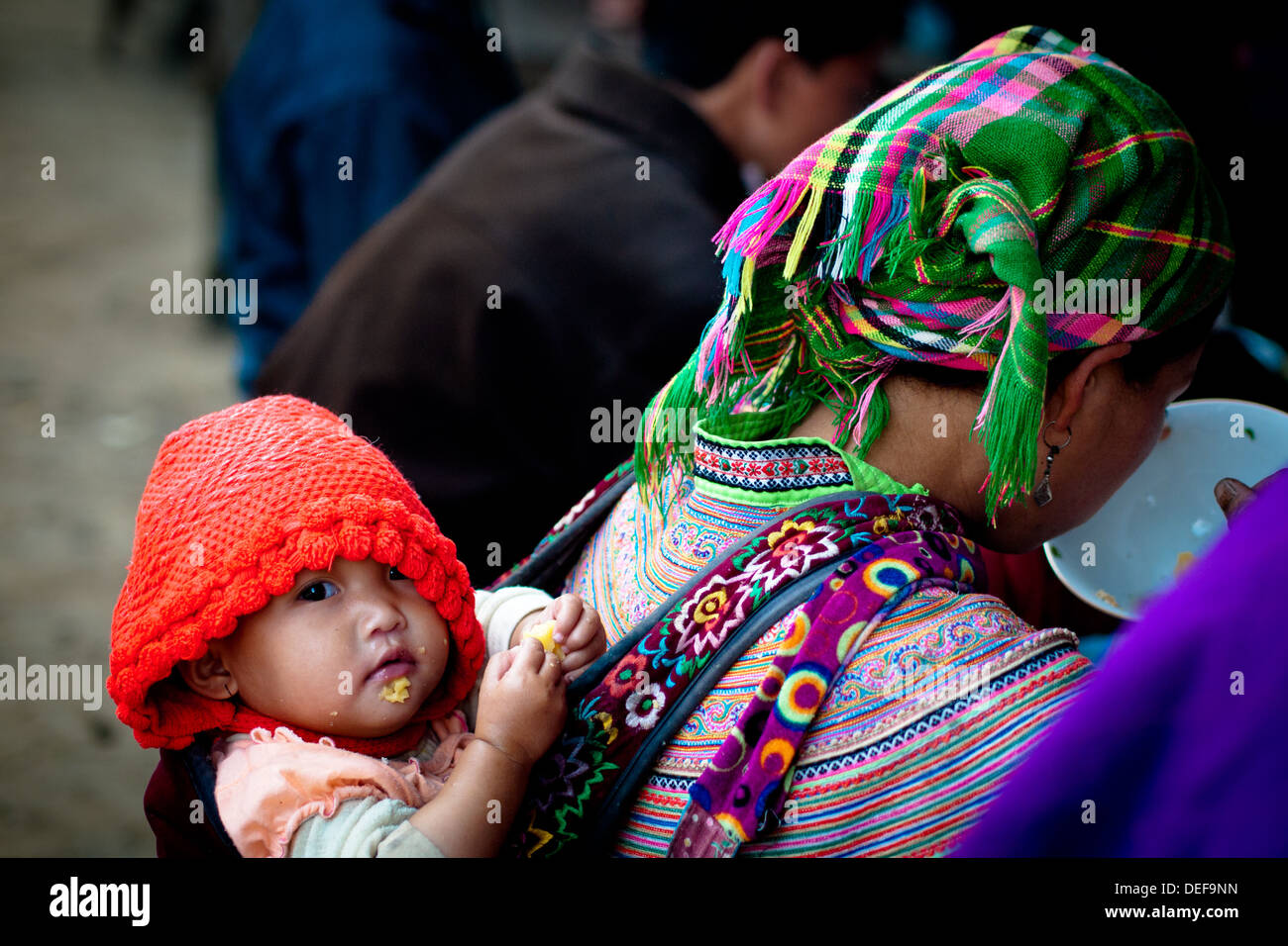 Ein Baby Flower Hmong blickt auf, während ihre Mutter Mittagessen am Sonntag Morgen Markt in Bac Ha, Provinz Lao Cai, Vietnam isst. Stockfoto