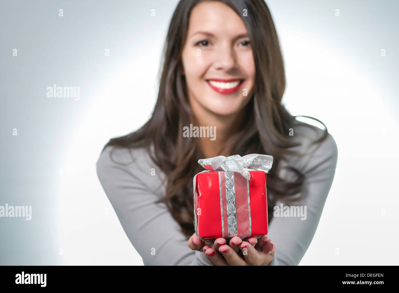 Hübsche junge Frau mit lange brünette Haare und eine schöne sanfte Lächeln hielt einen bunten roten Geschenk für einen lieben Menschen Stockfoto