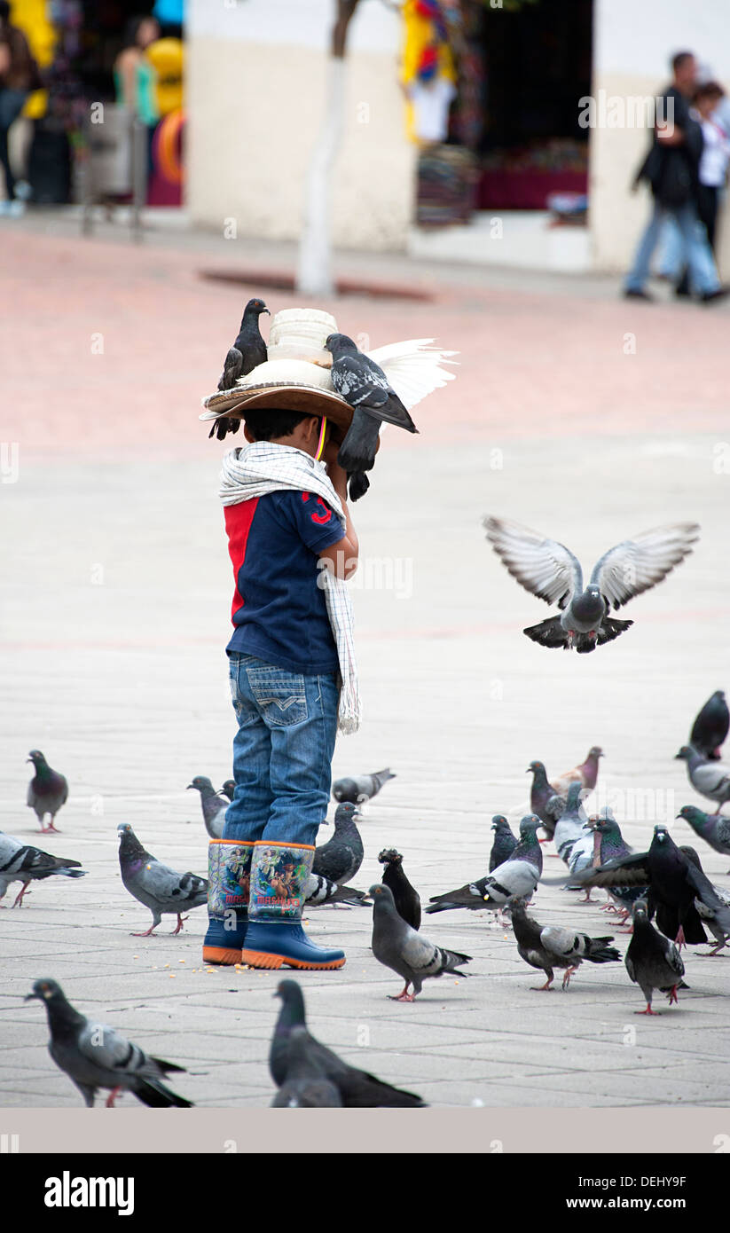 Kleiner Junge in Cowboystiefeln steht auf Platz mit Tauben am Hut. Fusagasuga, Kolumbien, Südamerika. Stockfoto