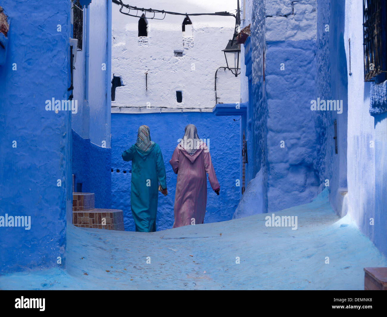 Zwei Frauen tragen traditionelle Kleidung zu Fuß in einer Straße mit blau gestrichenen Wänden in Chefchaouen, Marokko Stockfoto