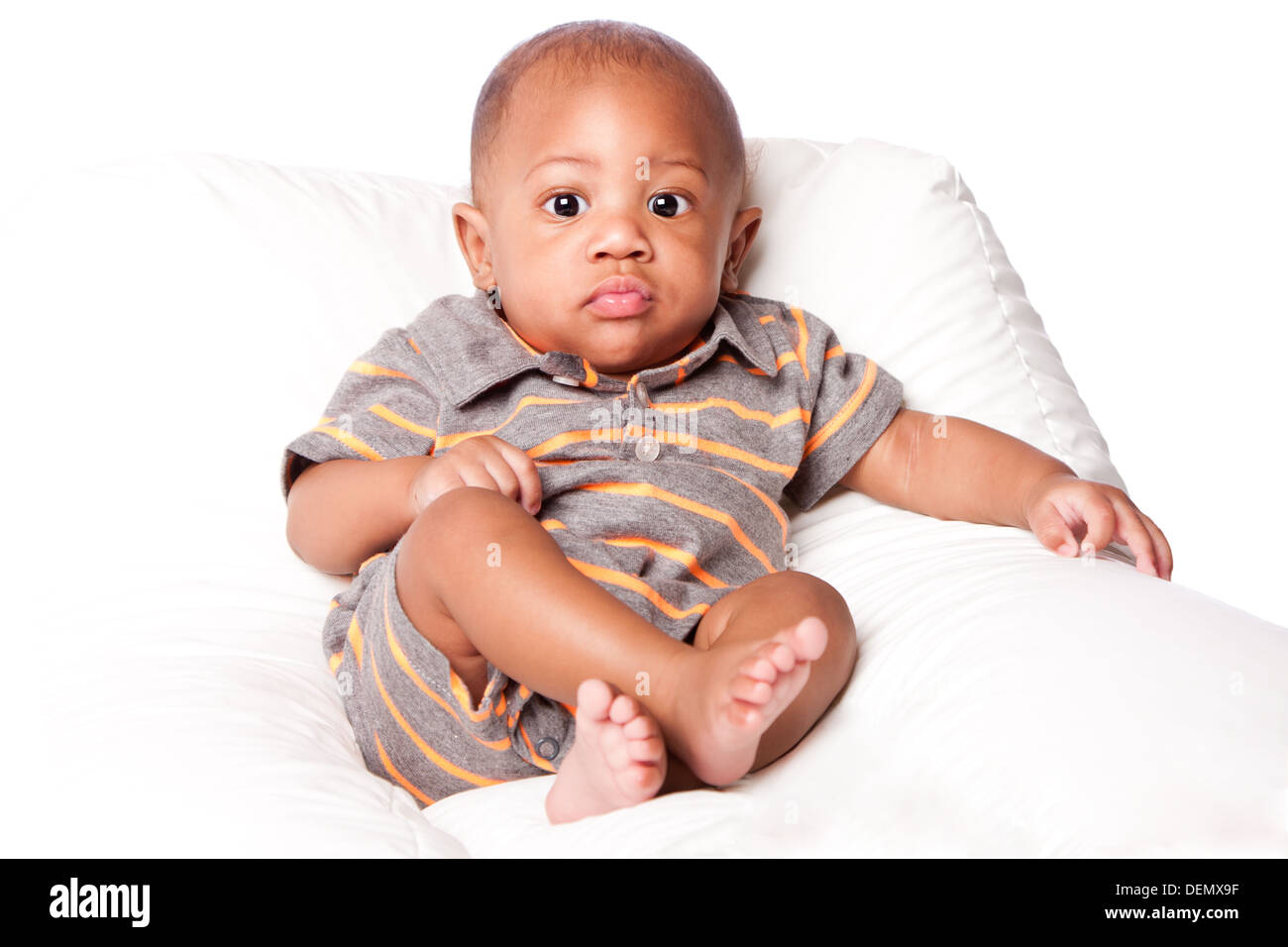 Schöne süße entzückende Baby Kleinkind sitzen entspannt trägt grau-Orange gestreifter Strampler Overall, auf weiß. Stockfoto