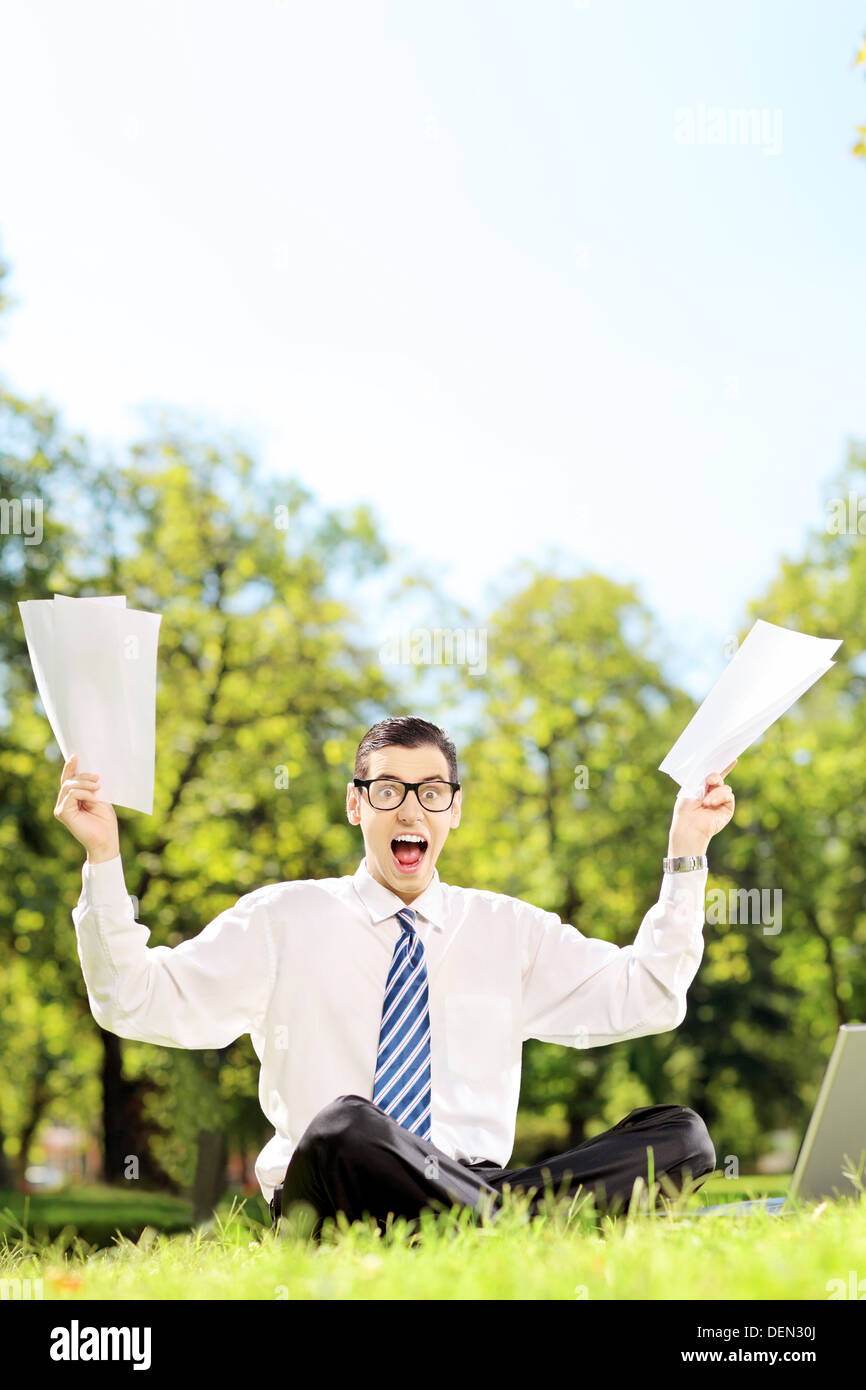 Angst junger Geschäftsmann Dokumente und schreien sitzen auf einer Wiese in einem park Stockfoto