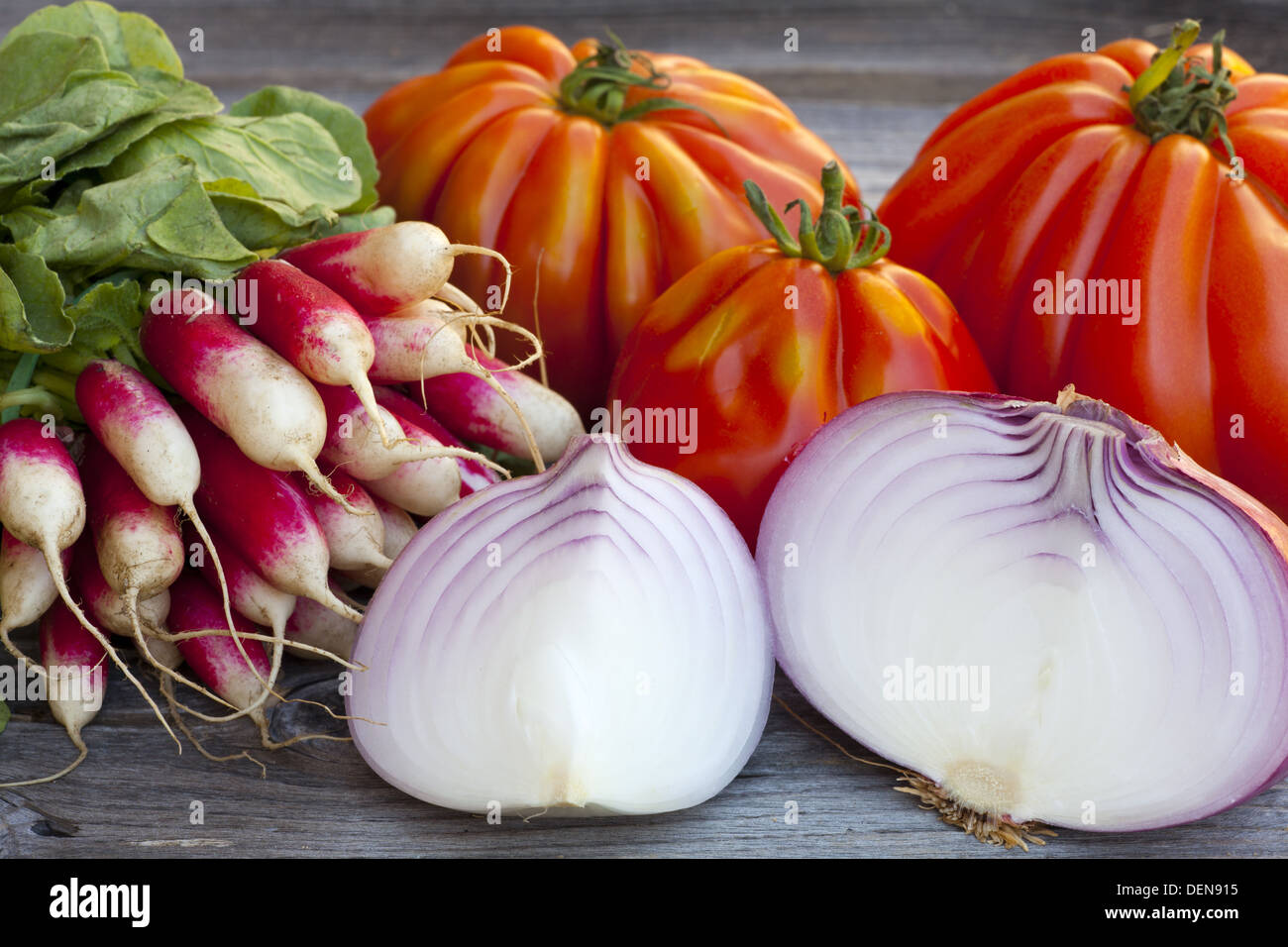 Coeur de Boeuf Tomaten, große rote Zwiebeln und Radieschen frisch vom Wochenmarkt auf einem alten Holztisch Stockfoto