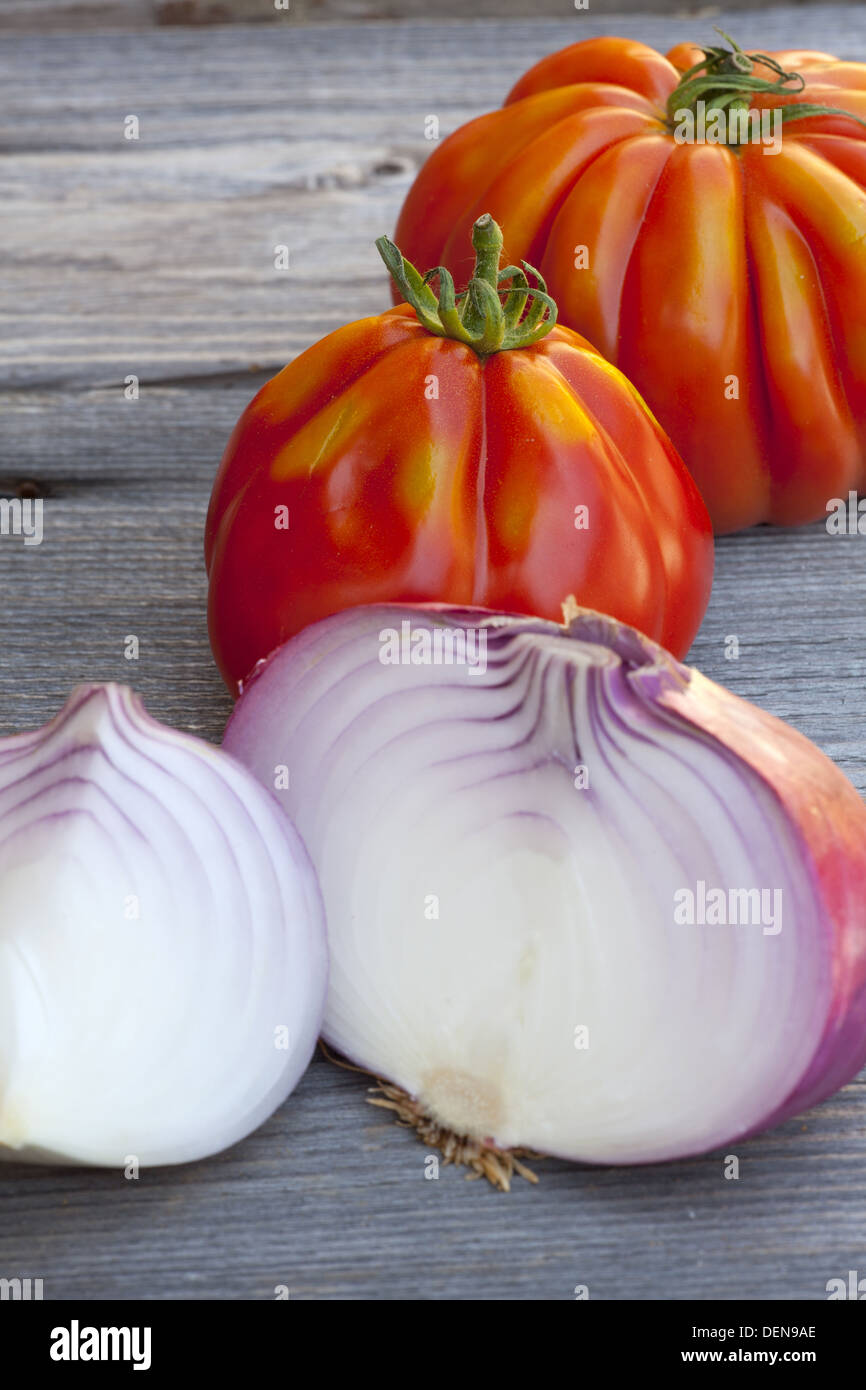 Coeur de Boeuf Tomaten und große rote Zwiebeln vom Wochenmarkt in Südfrankreich auf einem alten Holztisch Stockfoto