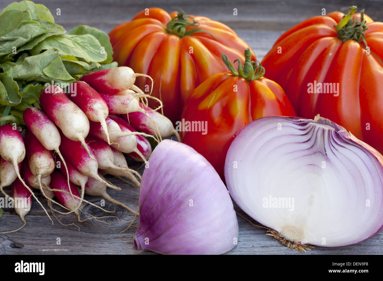 Coeur de Boeuf Tomaten, große rote Zwiebeln und Radieschen frisch vom Wochenmarkt auf einem alten Holztisch Stockfoto