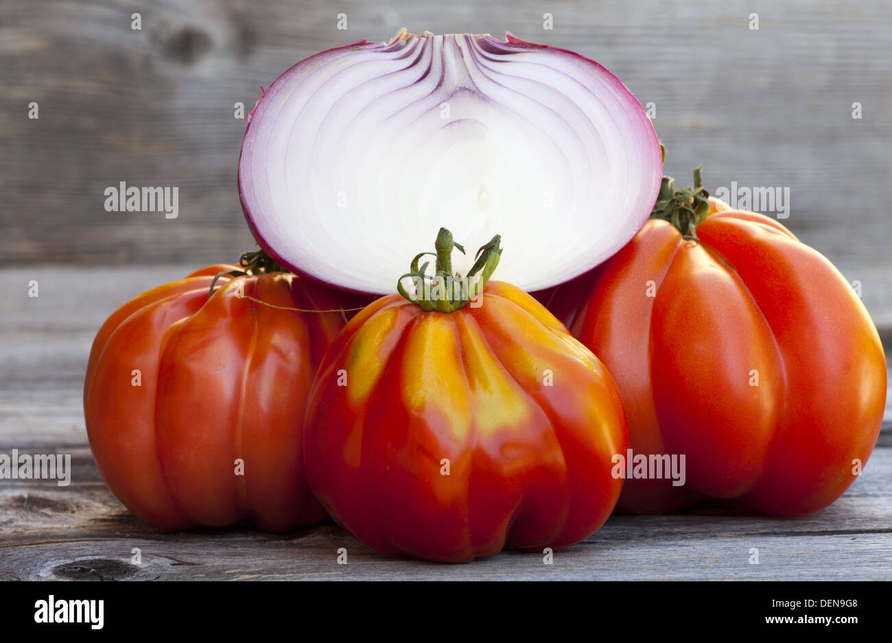 Drei Oxheart Tomaten und eine halbierte Zwiebel vom Wochenmarkt in Südfrankreich auf einem alten Holztisch Stockfoto