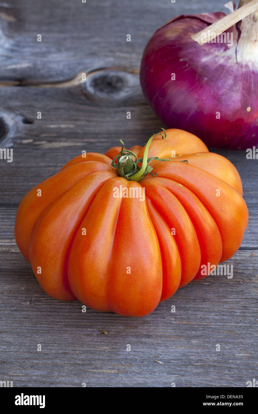 Ein Beefsteak Tomaten und eine ganze rote Zwiebel vom Wochenmarkt in Südfrankreich auf einem alten Holztisch Stockfoto