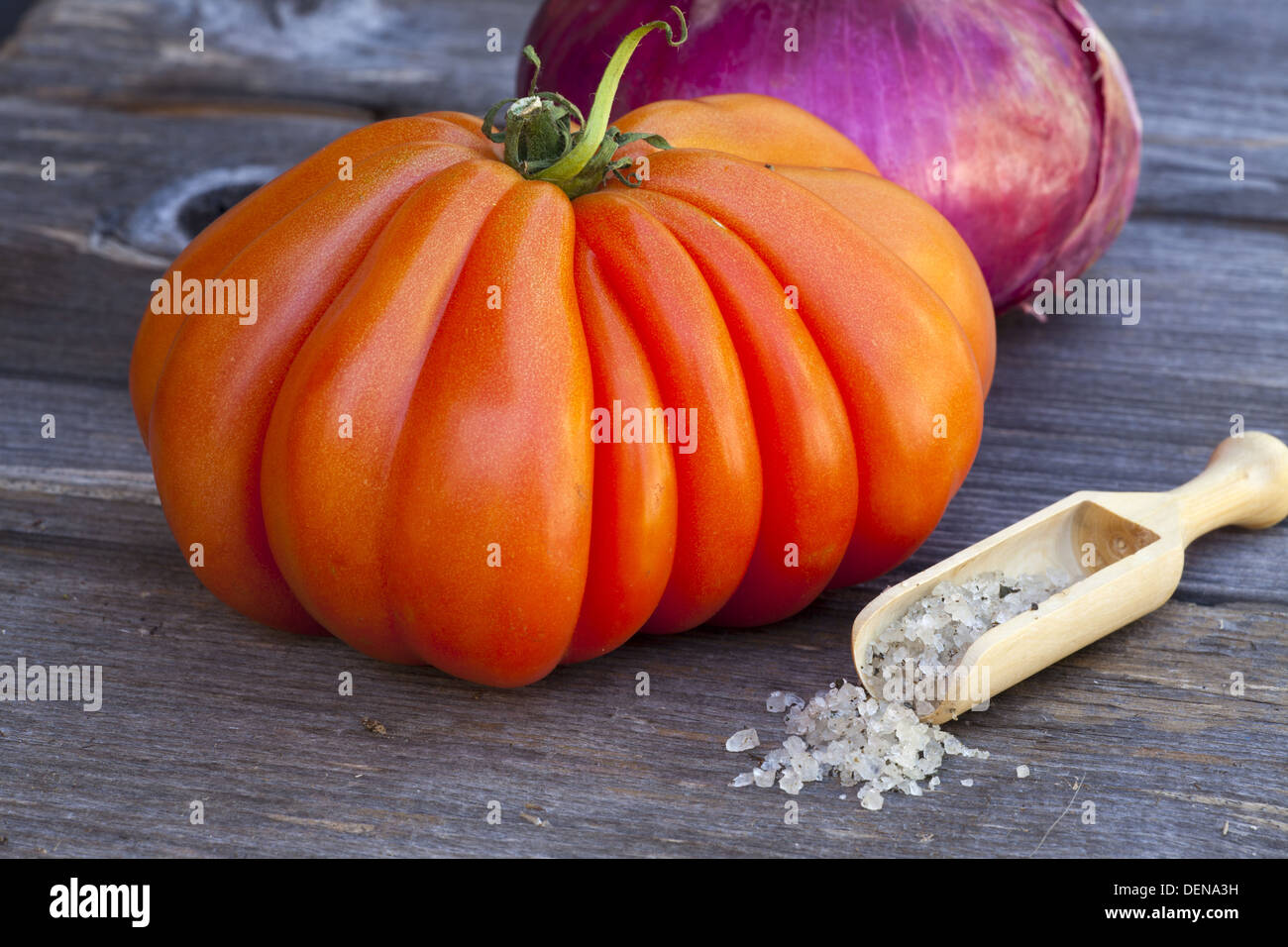 Coeur de Boeuf Tomaten und eine ganze rote Zwiebel mit Basilikum Meersalz in eine hölzerne Gewürz Kugel auf einem alten Holztisch Stockfoto