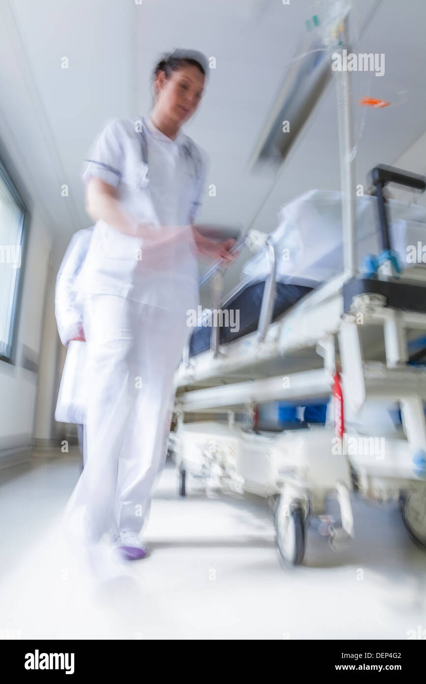 Bewegung verwischt Patienten auf Bahre Bahre mit Geschwindigkeit im Krankenhausflur durch Ärzte & Krankenschwestern in Notaufnahme geschoben Stockfoto