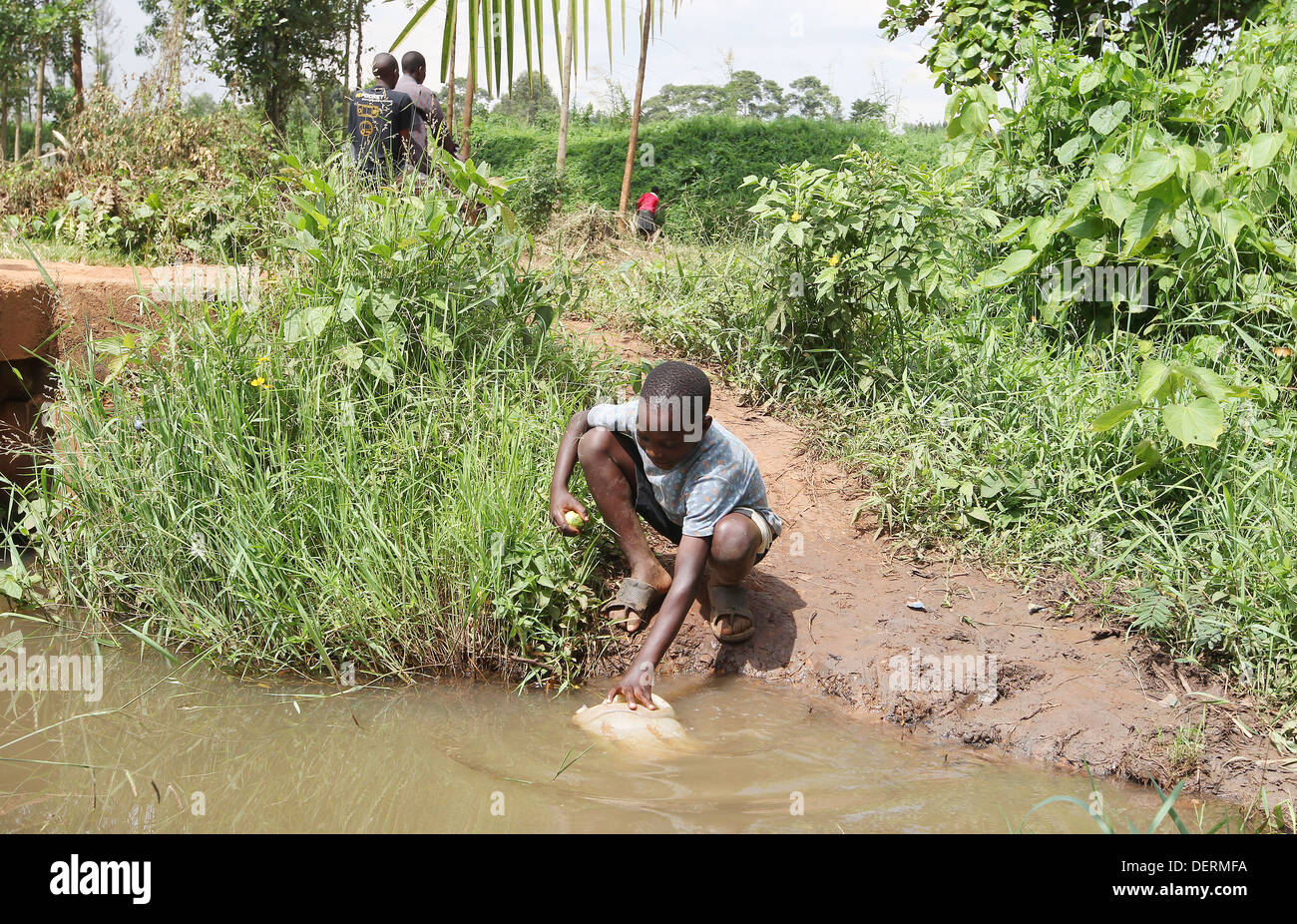 Ein kleiner Junge sammelt schmutziges Wasser aus einem Fluss im Luwero Distrikt von Uganda. Stockfoto