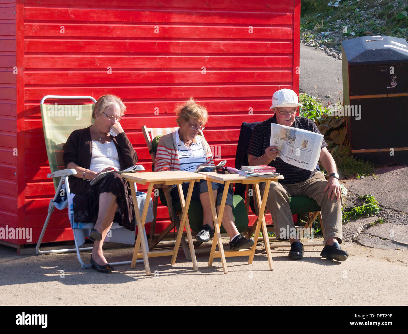Ein Mann und zwei Frauen lesen Sie ihre Zeitung in angenehmen Spätsommer-Sonne durch eine rote Strandhütte in Whitby Stockfoto