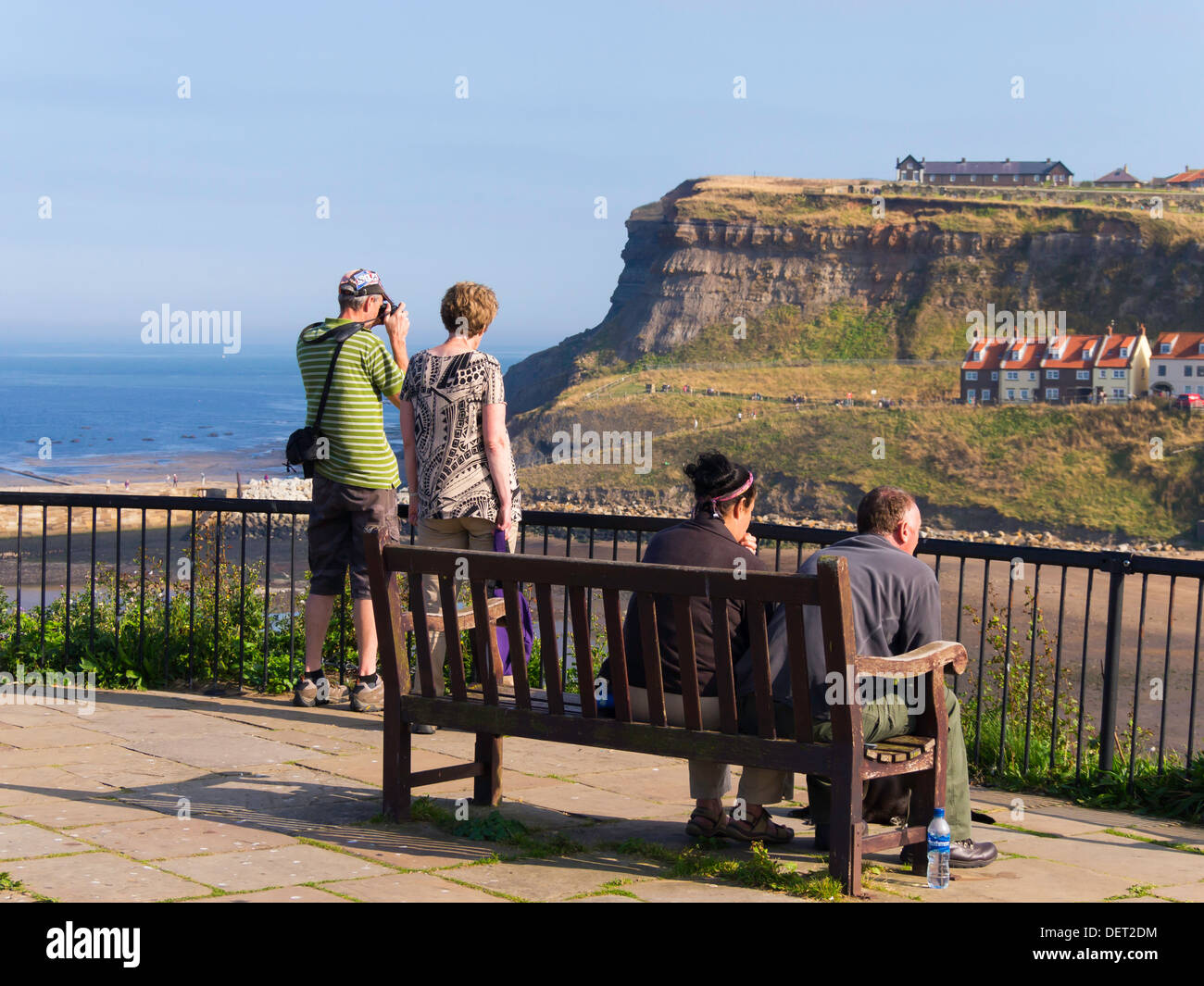 Touristen an einem Spätsommertag genießen Sie die Aussicht von einem Aussichtspunkt am Whitby West Cliff mit Blick auf den Hafen East Cliff Stockfoto