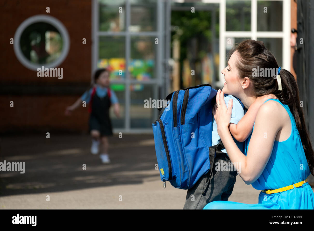 Eine attraktive junge Mutter beruhigend auf glücklich & Abholung oder Abwurf ihres Sohnes vor den Toren der Vorschule Stockfoto