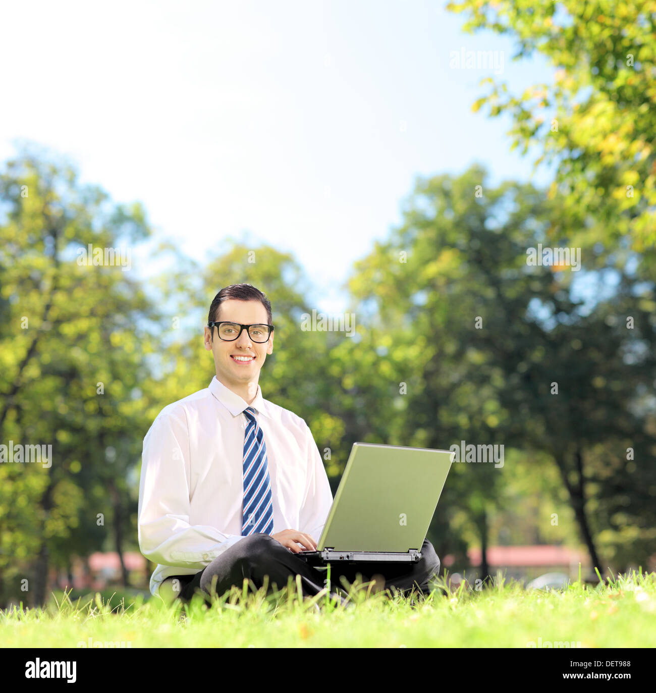 Junger Geschäftsmann auf einer grünen Wiese sitzen und arbeiten auf einem Laptop in einem park Stockfoto