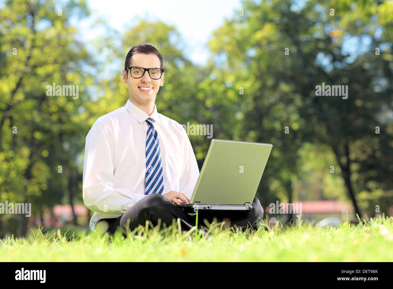 Junge Unternehmer mit Brille auf einer Wiese sitzen und arbeiten auf einem Laptop in einem park Stockfoto