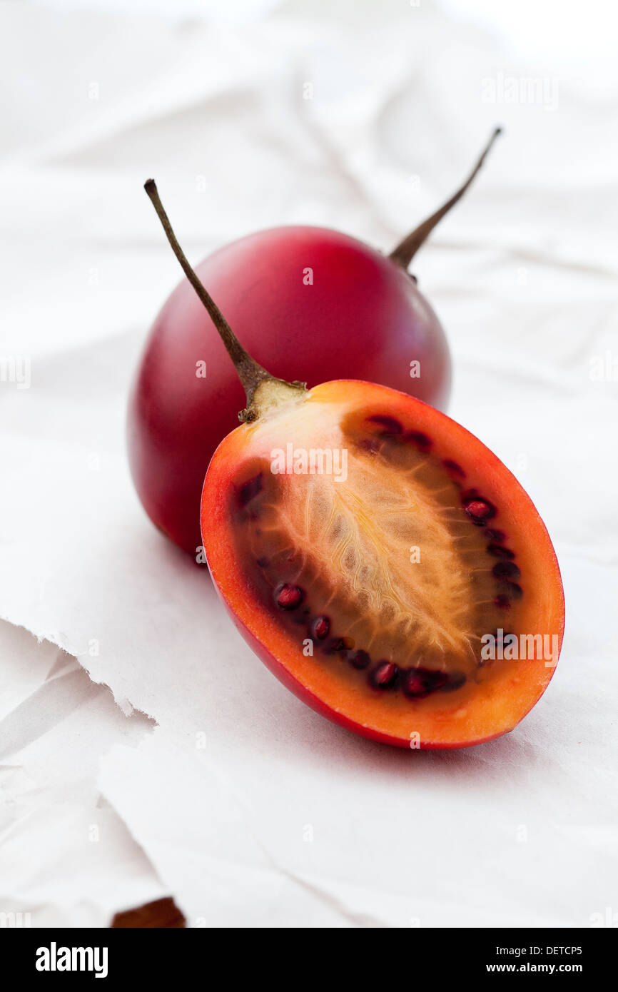 Eine in Scheiben geschnittene Tamarillo und ganzes eins auf ein weißes Papier-Oberfläche. Stockfoto