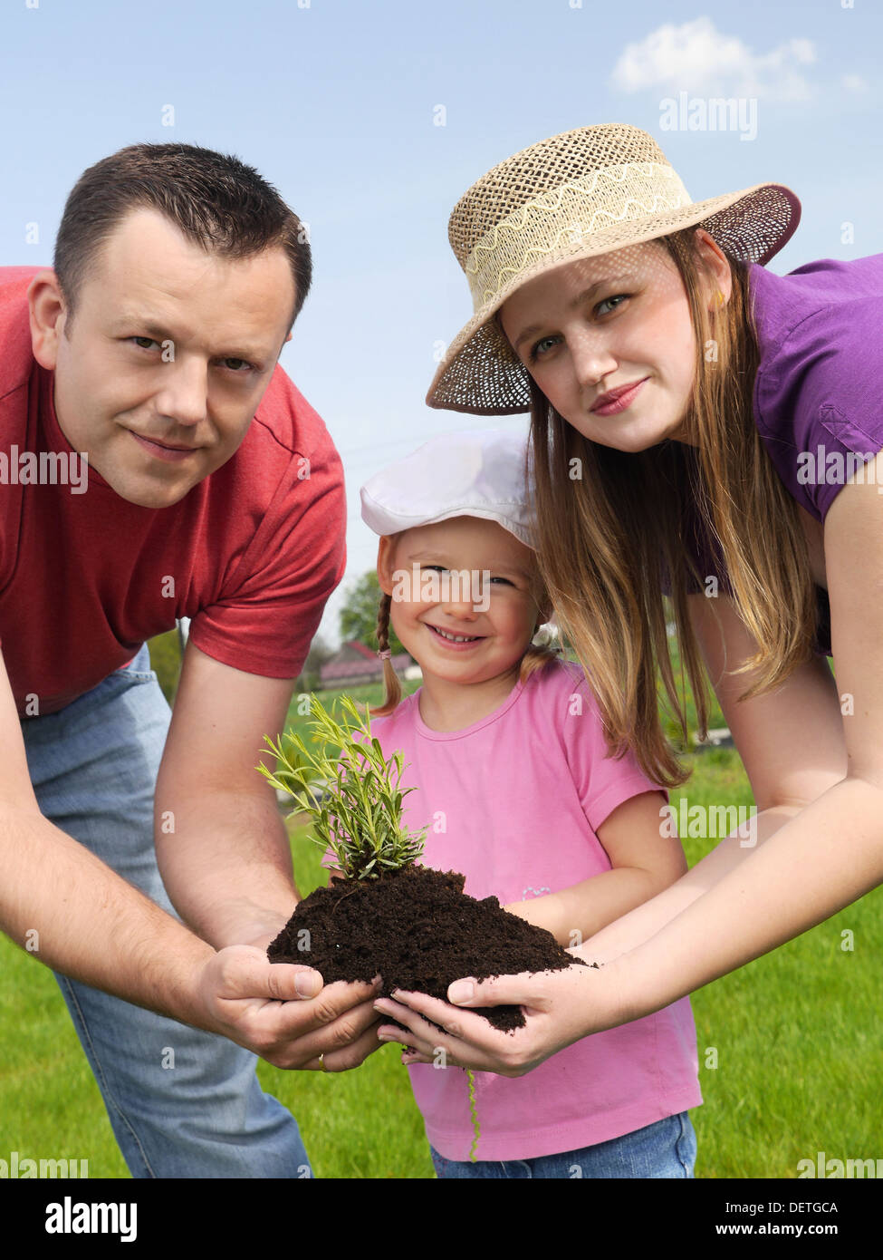 Papa, Mama und niedliche kleine Tochter zusammenhalten Handvoll Boden mit Pflänzchen Stockfoto