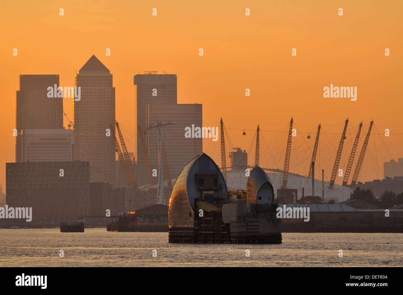 Die Thames Barrier, Canary Wharf und die O2 Arena bei Sonnenuntergang, von den Ufern der Themse in Woolwich, South East London, Großbritannien Stockfoto