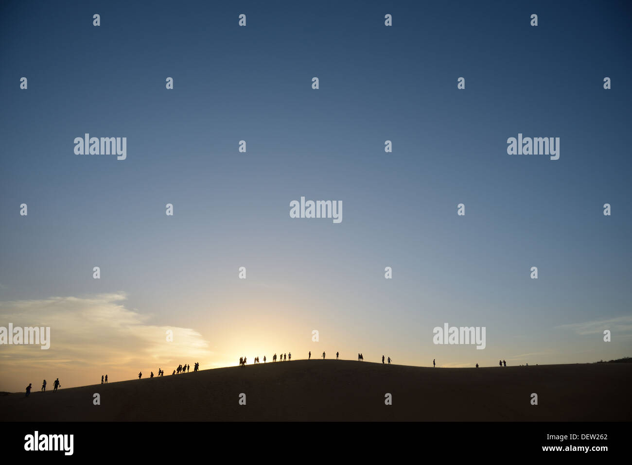 Gruppe von Personen auf große Sanddüne am Horizont die untergehende Sonne beobachten. Stockfoto