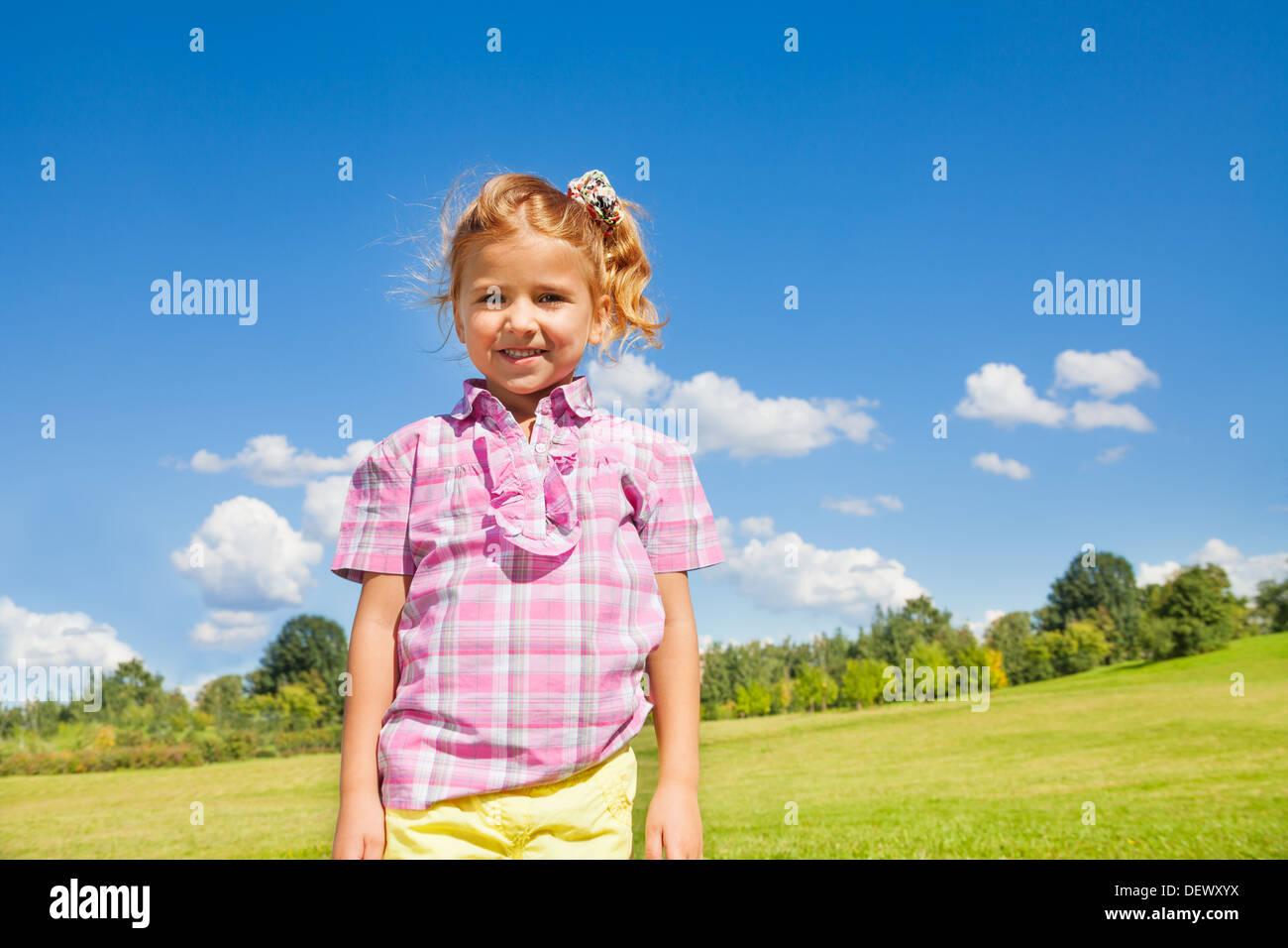 Schönes Lächeln wenig 5 Jahre altes Mädchen im rosa Hemd stehen mit Himmel und Park am sonnigen Tag Stockfoto
