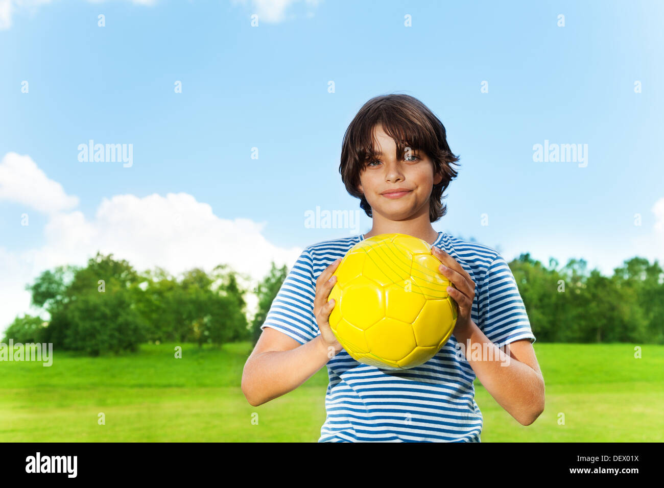 Porträt des 14 Jahre alten Jungen halten Fußball auf dem Feld an sonnigen Tag Stockfoto