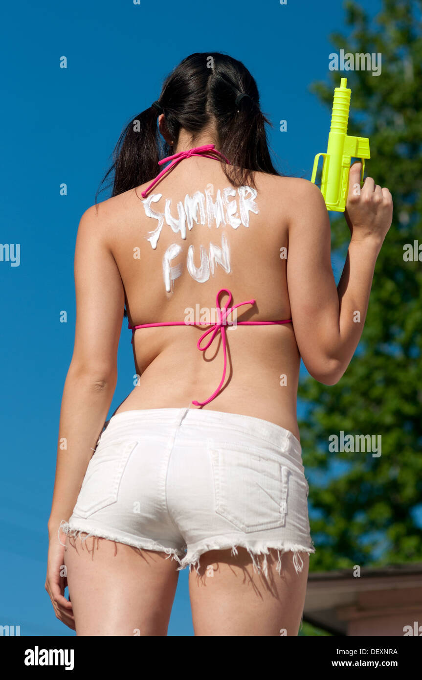 Frau Rückansicht mit Sonnenschutz Lotion schreiben hält Wasserpistole Sommer Spaß Stockfoto