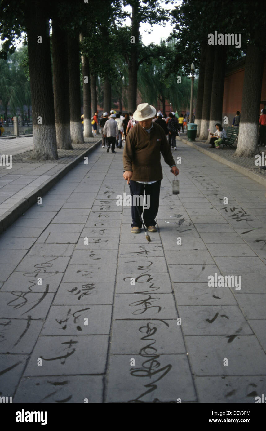 Ein Mann nutzt einen manipulierten riesigen Pinsel Tinte Wasser verdunstet wie Kalligraphie, die verschwindende Tinte auf der Fahrbahn in Summer Palace Beijing China zu schreiben. Stockfoto Ein Mann nutzt einen manipulierten riesigen Pinsel Tinte Wasser verdunstet wie Kalligraphie, die verschwindende Tinte auf der Fahrbahn in Summer Palace Beijing China zu schreiben. Stockfoto