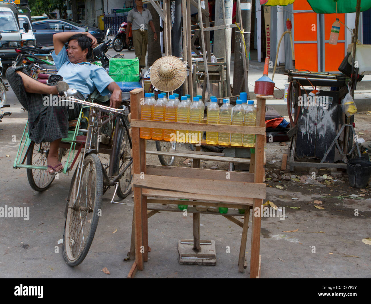 Ein Dreirad-Rikscha-Fahrer wartet auf einen Tarif in der Nähe einer Tankstelle in zentralen Mandalay, Birma. Stockfoto
