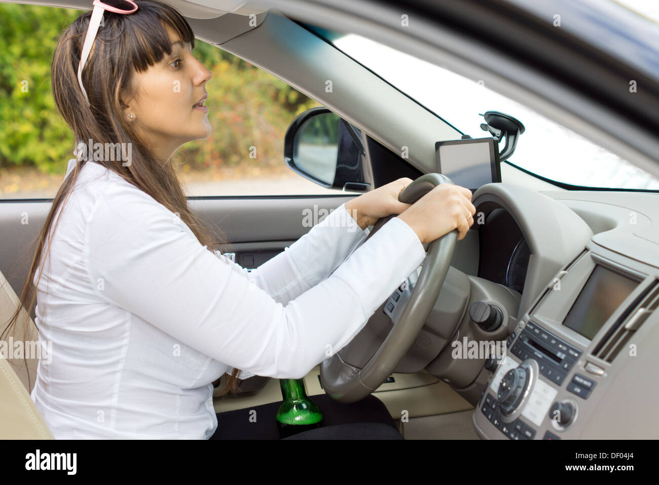 Betrunkene Fahrerin versucht, beurteilen ihre Distanzen umklammert ihre Flasche Schnaps zwischen ihre Schenkel und steigen bis über das Dashboard zu spähen. Stockfoto