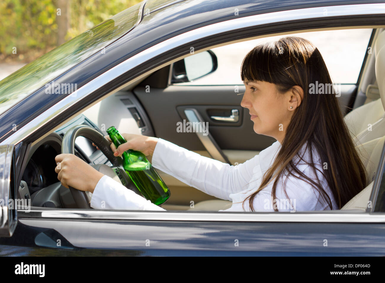 Betrunken Frau Fahrer lächelnd wie sie mit einer Flasche Alkohol fest in einer Hand hielt fährt durch das Seitenfenster anzeigen Stockfoto