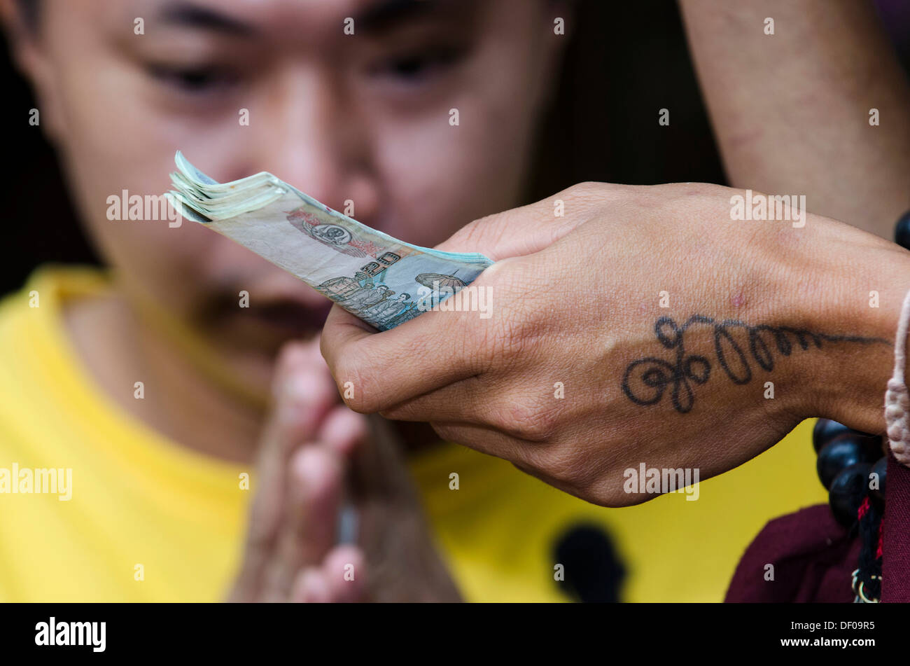 Charme-Verkauf, Mann, der die traditionelle Geste von Gruß und zeigen Respekt, Wai, tätowiert Hand Holding Banknoten, Tempel Stockfoto