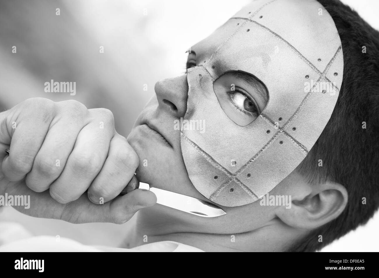 monochrome ernsten jungen Mann in Spuk Maske mit Messer Stockfoto