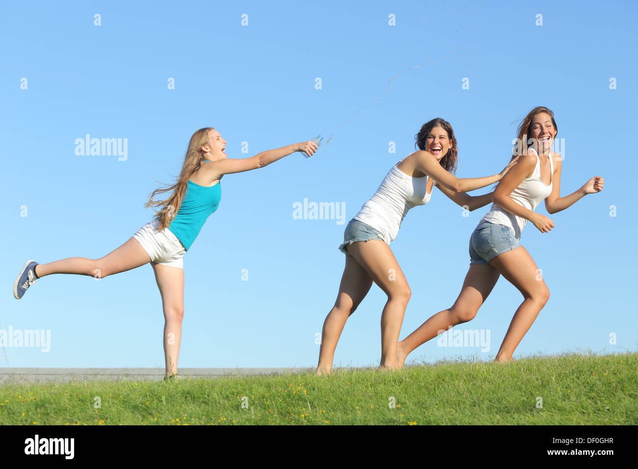 Gruppe von Teenager-Mädchen spielen glücklich werfen Wasser auf dem Rasen mit dem Himmel im Hintergrund Stockfoto