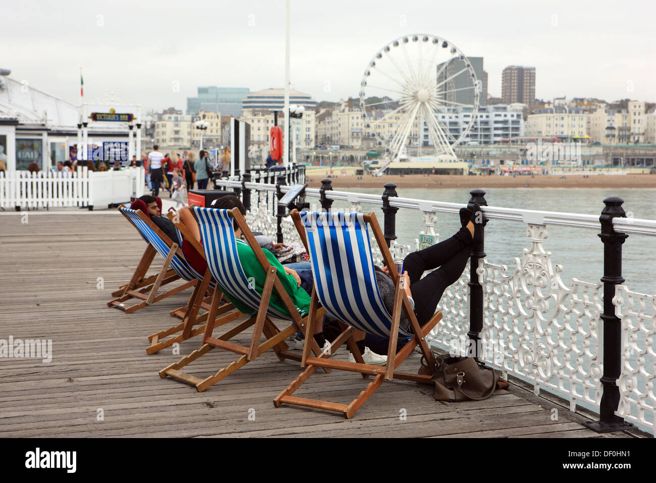 Jugendliche, die entspannend auf Liegestühlen am Pier von Brighton in East Sussex, England Stockfoto