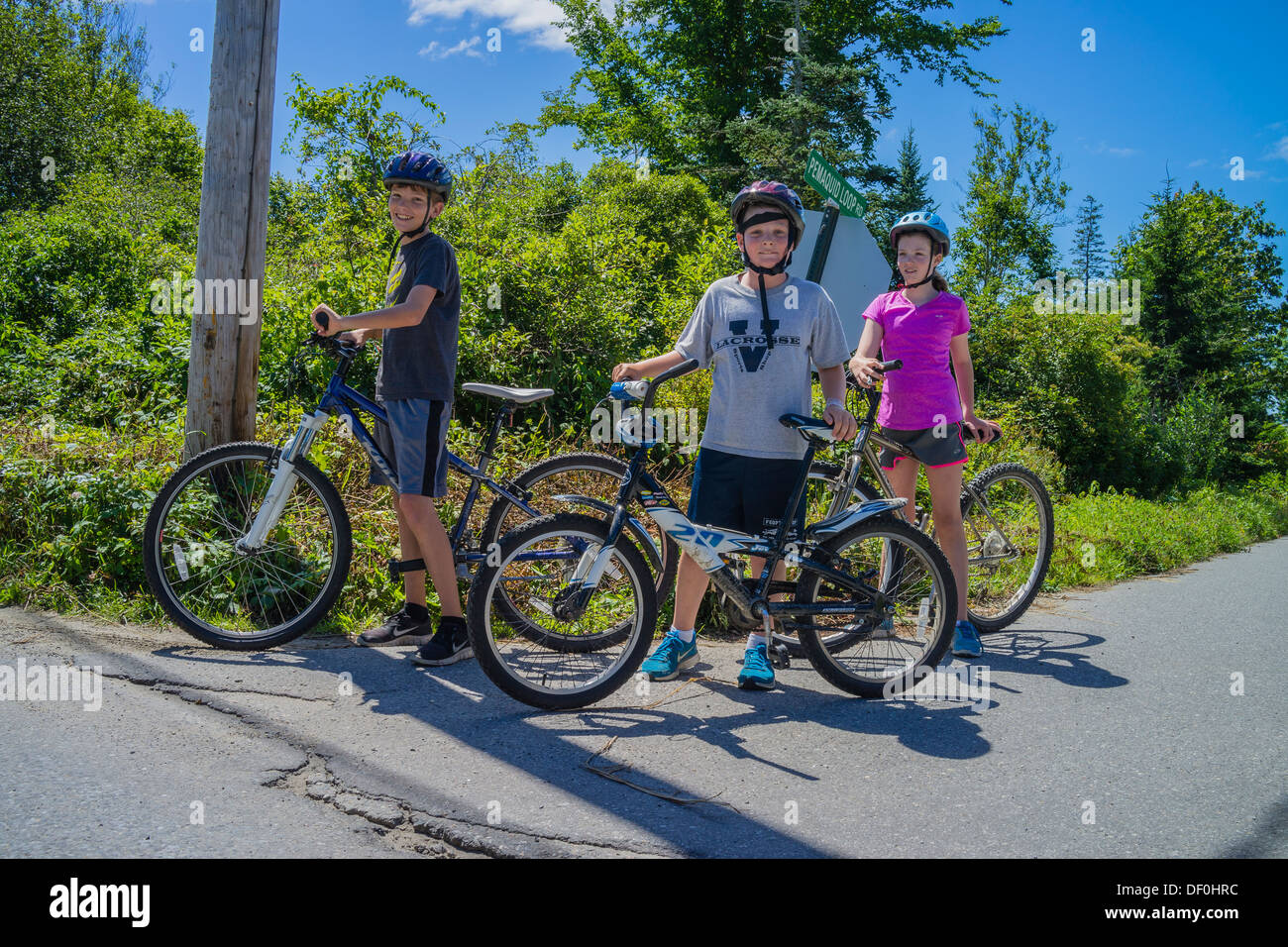 Zwei 12-13 Jahre alten Jungen und ein Mädchen für einen Moment innehalten und ihre Fahrräder während ihrer Sommerferien von der Schule stehen. Stockfoto