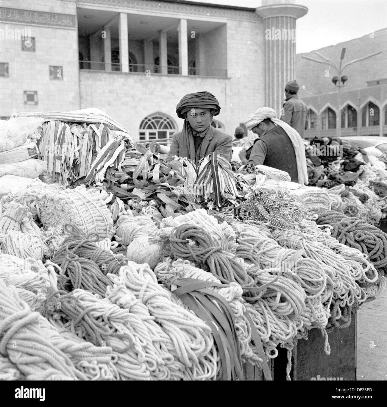 Historisches Bild aus den 1950er Jahren von J Allan Cash, von einem jungen afghanischen Jungen mit dem traditionellen Kopfteil, einem Turban, der neben seinem Marktstand steht und Seilbüschen und Garne zeigt, Kabul, Afghanistan. Stockfoto