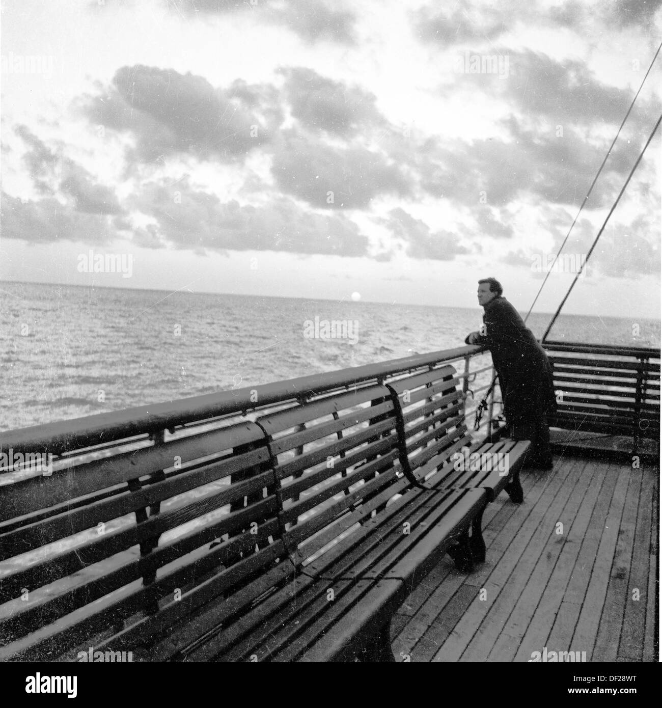 1950er Jahre, historisch, am frühen Abend und ein erwachsener Mann auf eigene Faust, der auf eine Barriere mit Blick auf die Weite des Meeres am Ende eines Schiffsdecks lehnt. Stockfoto