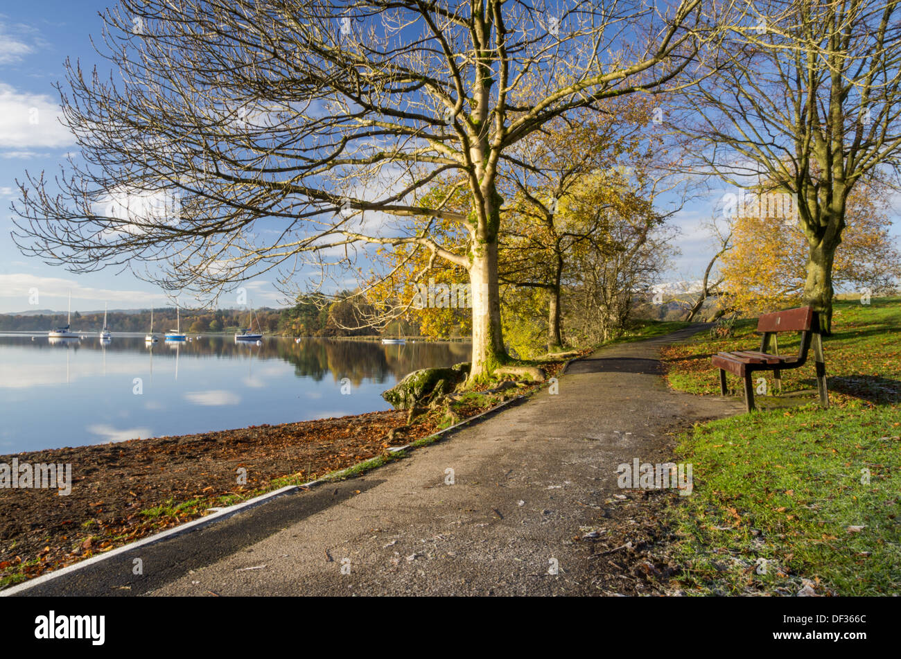 Eine ruhige Szene aus einer Bank in einem Park am See in der Nähe von Ambleside an einem sonnigen Morgen mit spiegelglatte Wasser und Yachten. Stockfoto