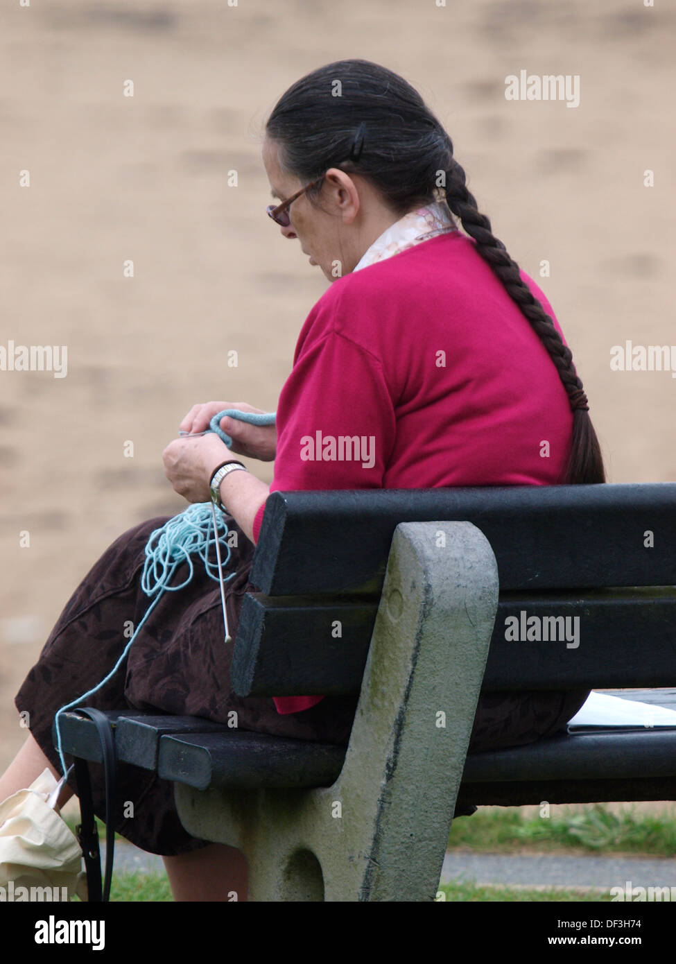 Alte Frau saß auf einer öffentlichen Bank, stricken, UK Stockfoto