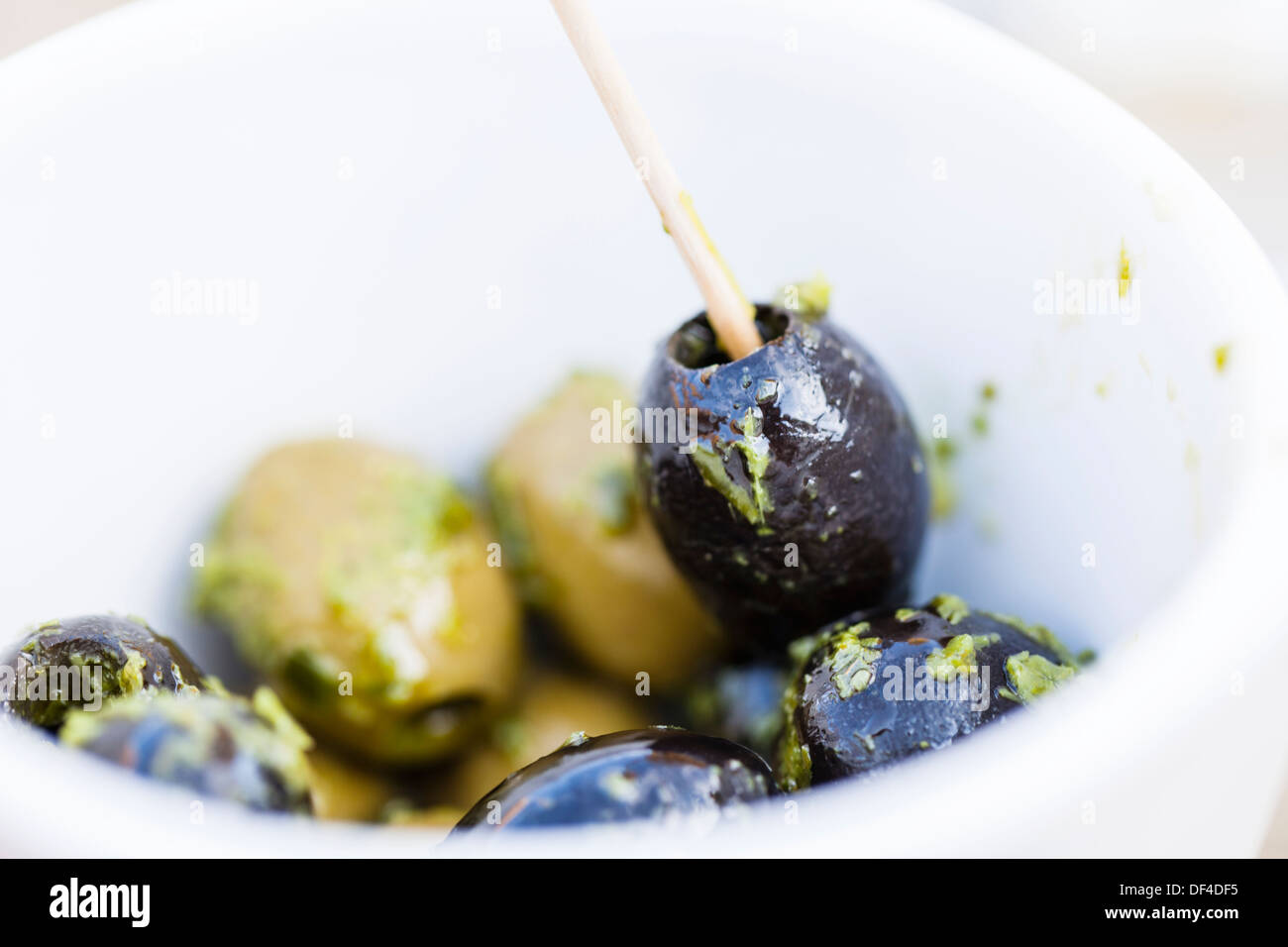 Schwarze und grüne Oliven in kleine Schüssel mit Öl und Kräuterdressing. Eine Olive ist mit einem hölzernen Pick ausgewählt. Stockfoto