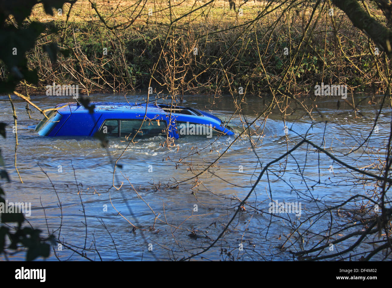 Ein kleines blaues Auto gefangen und teilweise in einen schnell fließenden angeschwollenen Fluss getaucht. Stockfoto