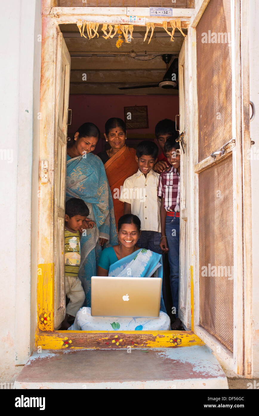 Ländliche Indianerdorf Frauen und Familie auf der Suche auf einem Apple-Laptop in ihrem Haus Tür. Andhra Pradesh, Indien Stockfoto