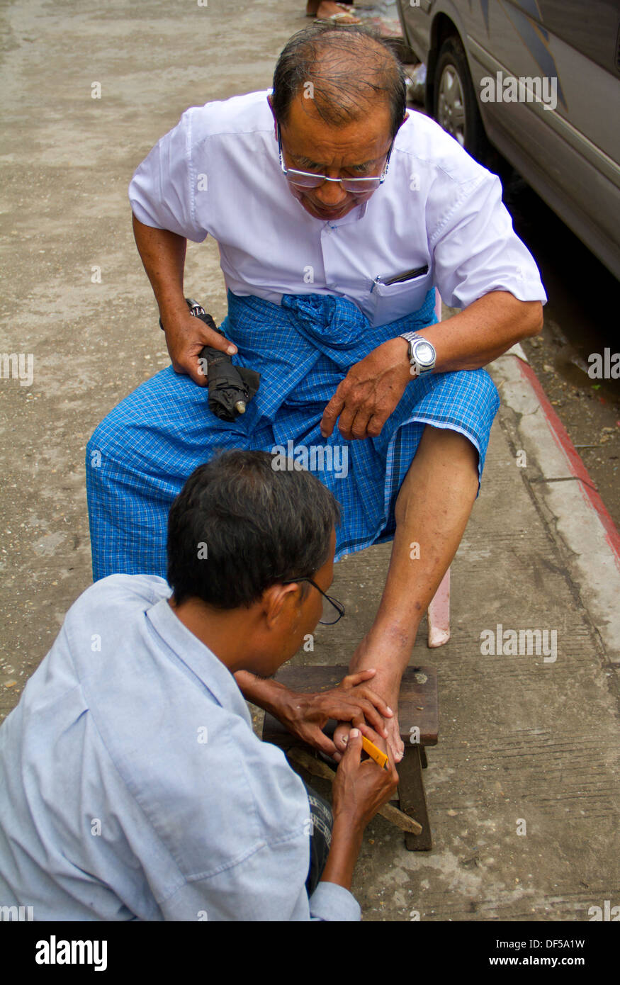 Einen Mann bekommen seine Fußnägel auf dem Bürgersteig in Yangon, Birma gewartet. Stockfoto