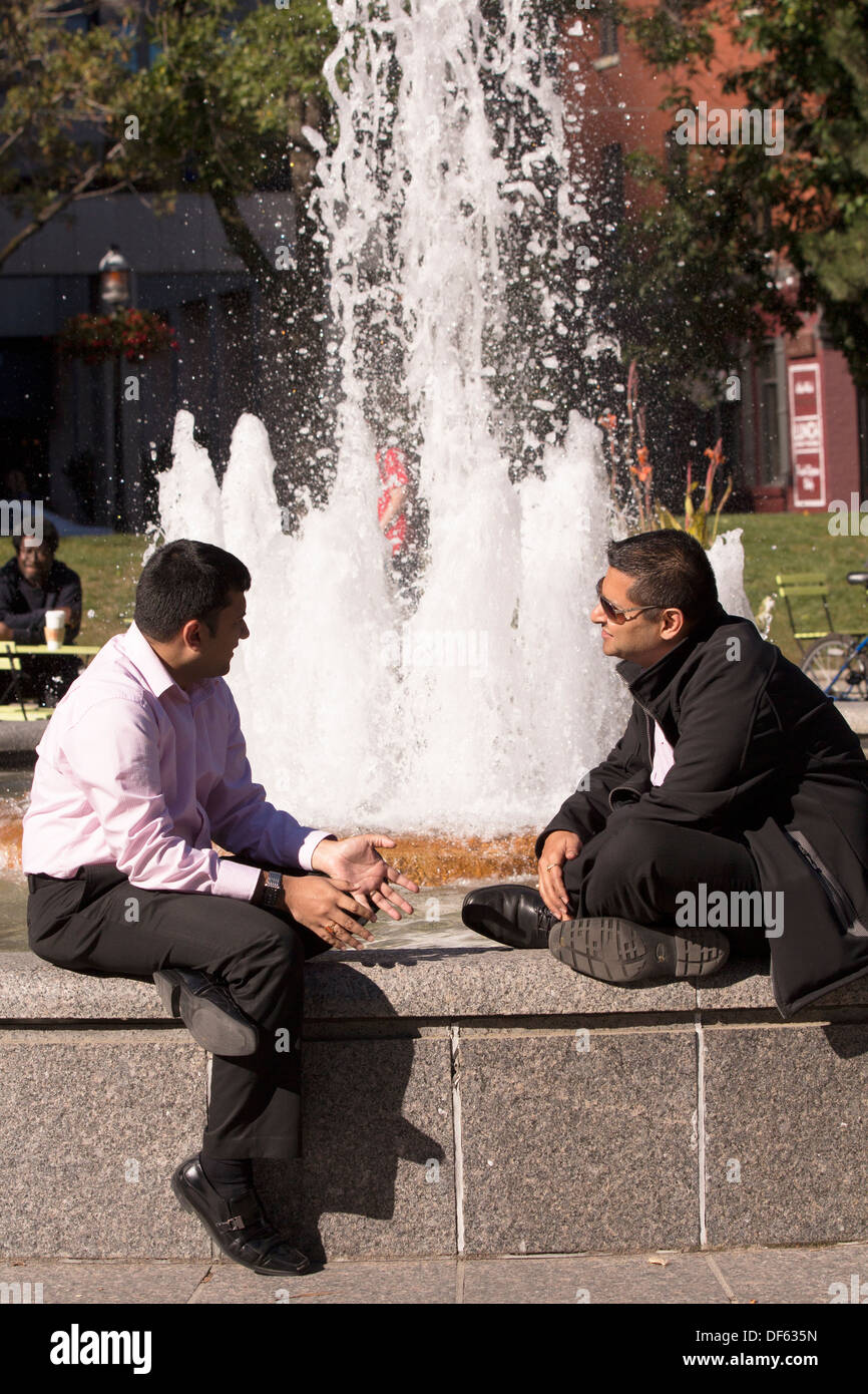 Unternehmer im Gespräch sitzt auf der Mauer vor Brunnen im Berczy Park in Toronto, Ontario Stockfoto