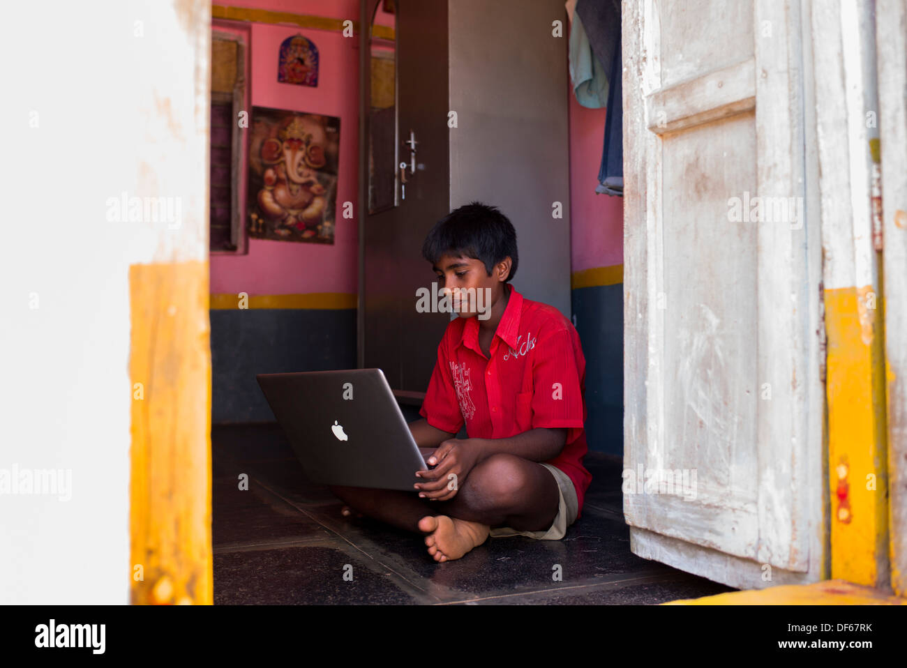 Indische Bauerndorf Jugendlicher Blick auf einem Apple-Laptop in seinem Haus Tür. Andhra Pradesh, Indien Stockfoto