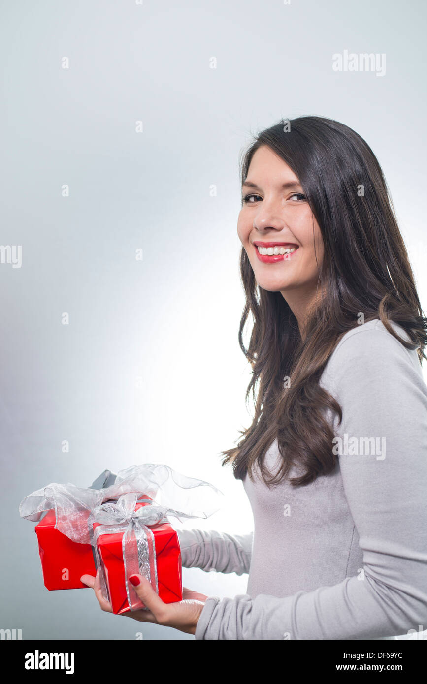 Hübsche junge Frau mit lange brünette Haare und einen schönen sanften Lächeln durchhalten bunte rote Geschenke für einen lieben Menschen Stockfoto