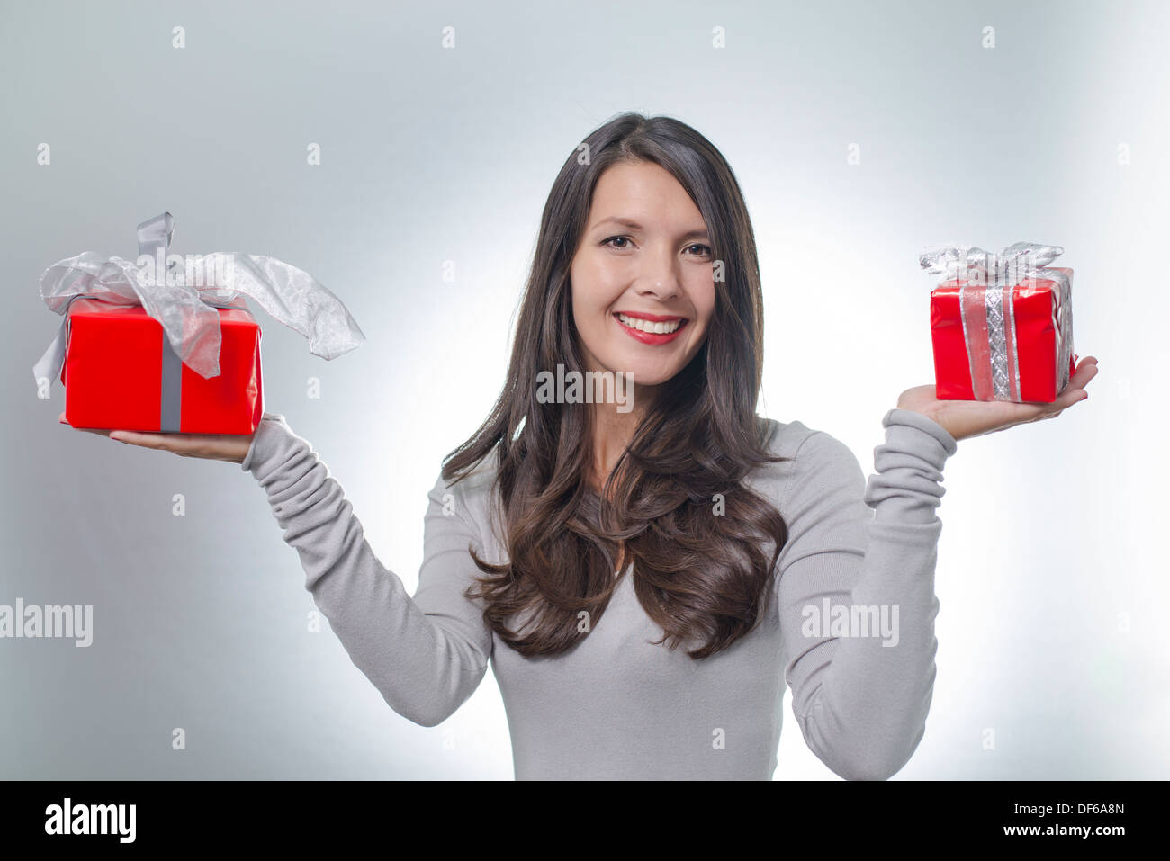 Hübsche junge Frau mit lange brünette Haare und einen schönen sanften Lächeln durchhalten bunte rote Geschenke für einen lieben Menschen Stockfoto