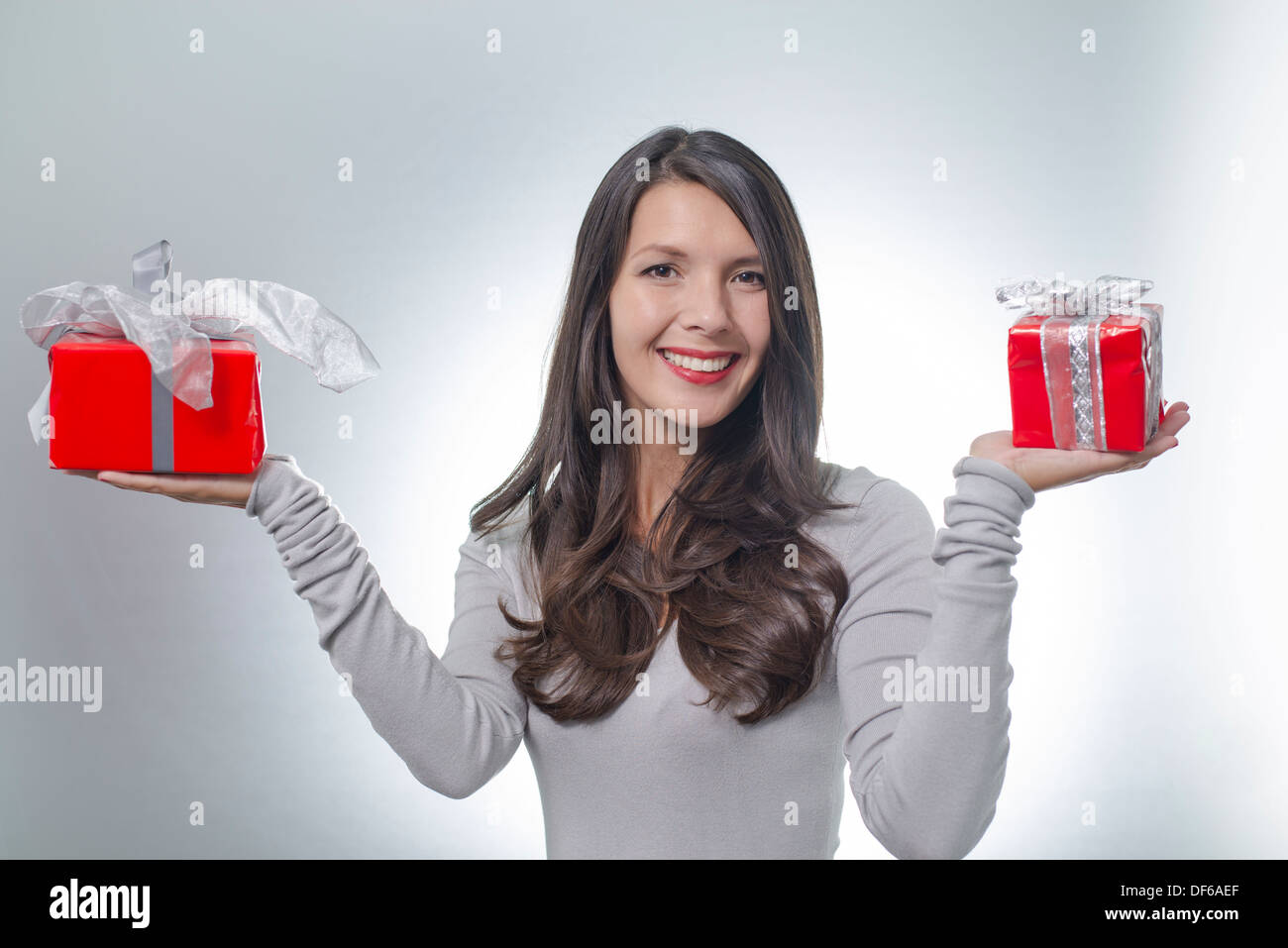 Hübsche junge Frau mit lange brünette Haare und einen schönen sanften Lächeln durchhalten bunte rote Geschenke für einen lieben Menschen Stockfoto