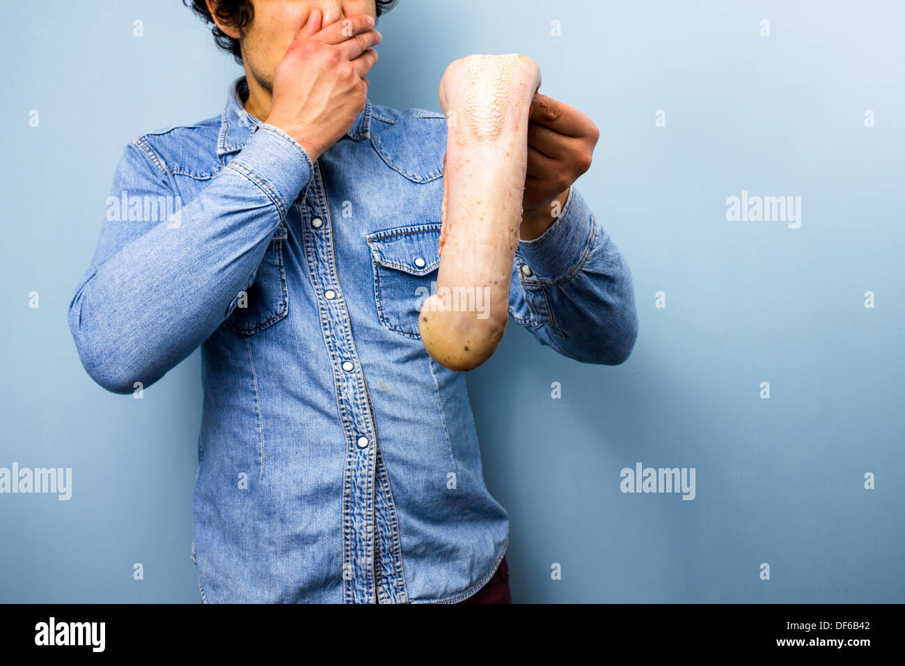 Junger Mann ist angewidert von rohen Ochsenzunge, die er in der Hand Stockfoto